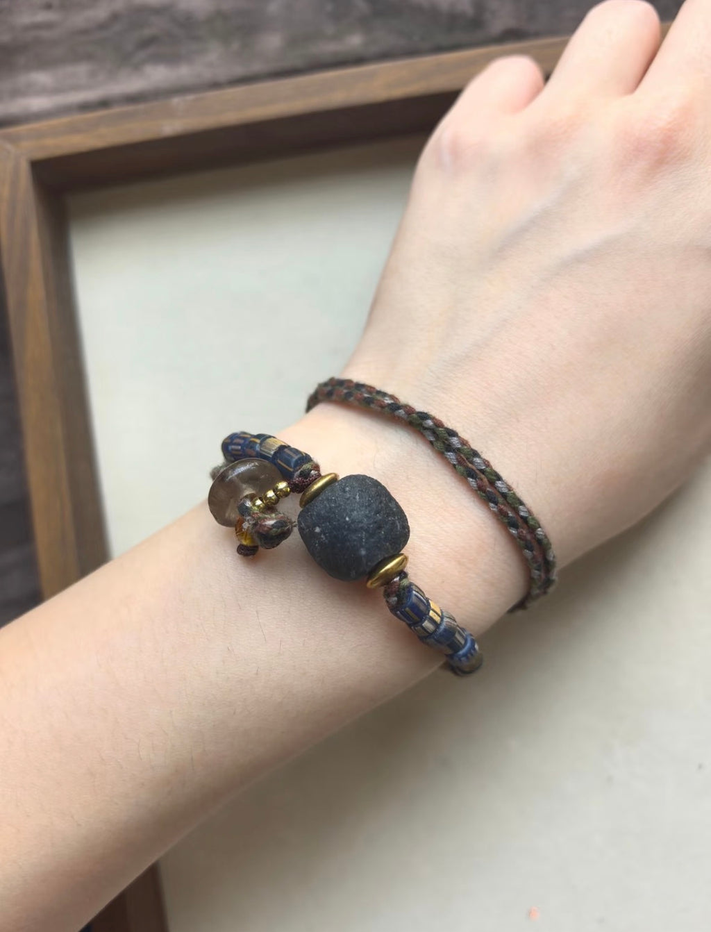 Handmade convertible necklace bracelet wrapped on wrist with dark focal bead, braided cord, and blue striped beads