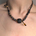 Handmade adjustable beaded cord necklace with dark focal bead, indigo striped beads, and brass accents worn as a short necklace