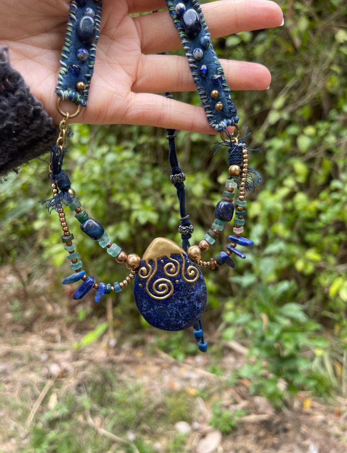 Close-up of a handmade blue stone pendant necklace showing bead detail, cord structure, and a sculptural pendant.