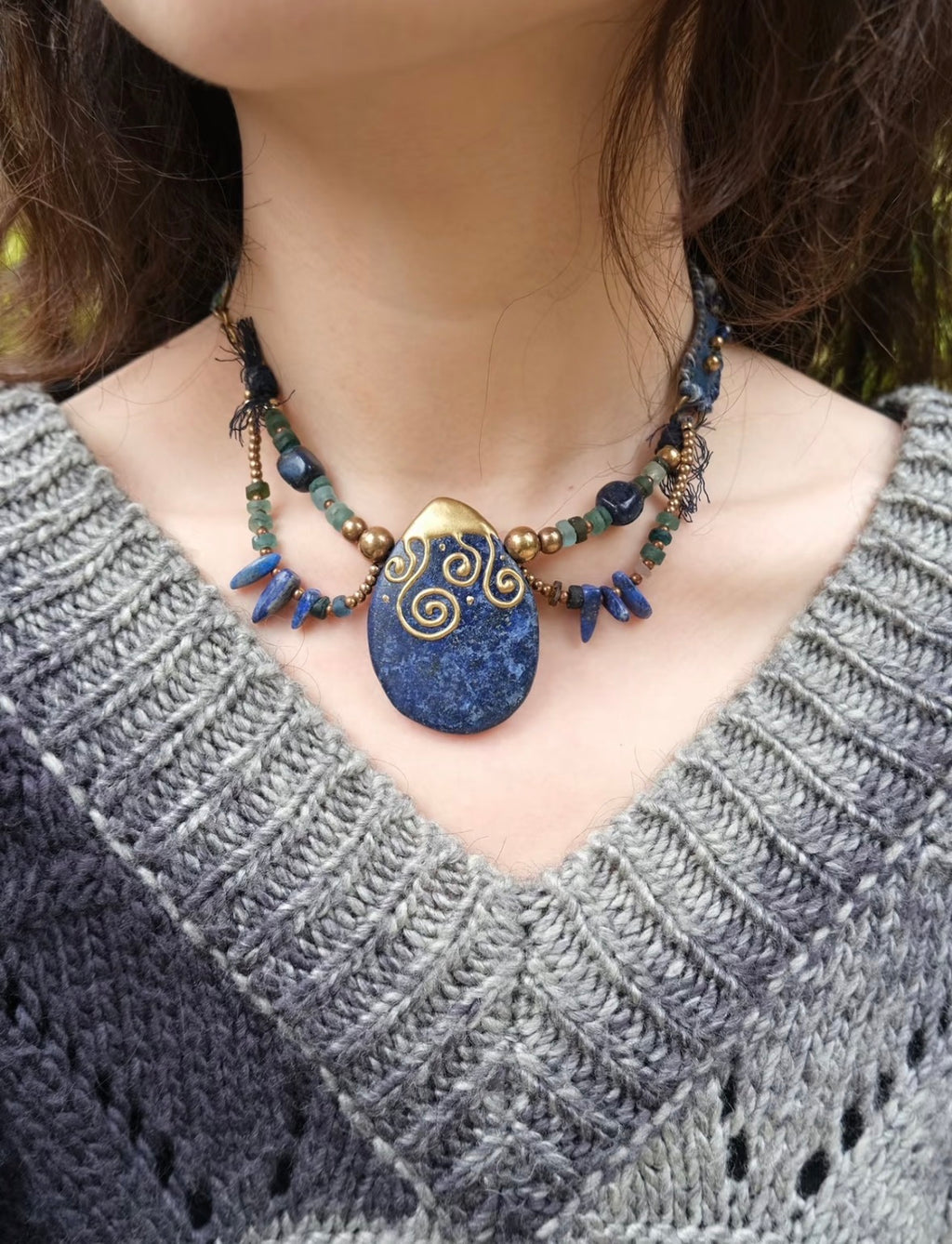 Model wearing a handmade blue stone pendant necklace with artisan beadwork and textile details.