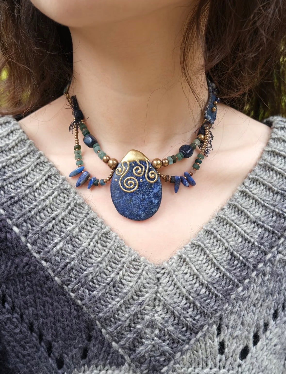Model wearing a handmade blue stone pendant necklace with artisan beadwork and textile details.