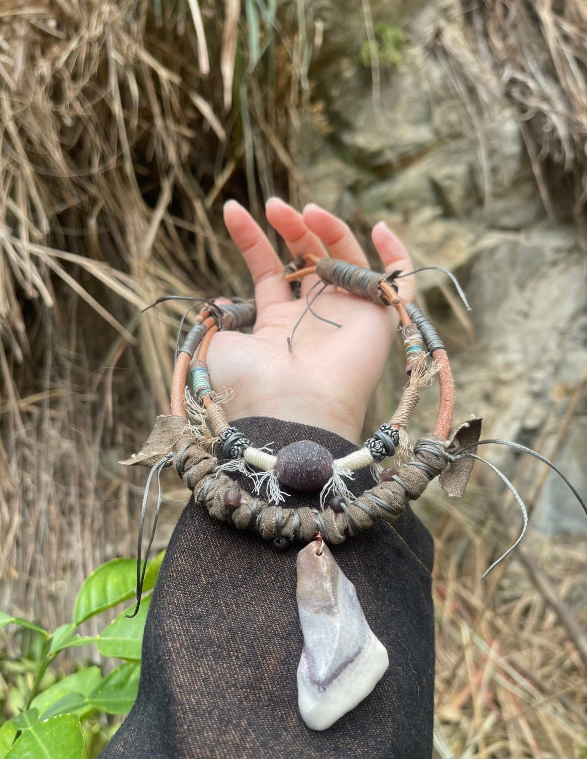 One-of-a-kind pendant necklace held outdoors with natural bohemian texture
