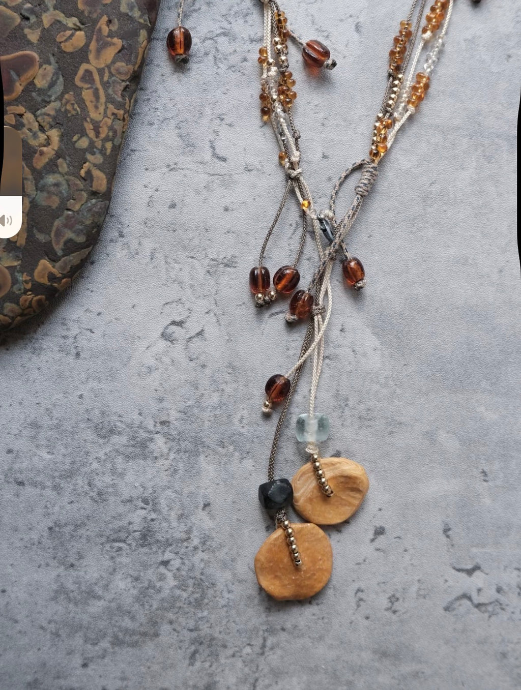 Detail view of a handmade brass pendant necklace with cord and bead accents.