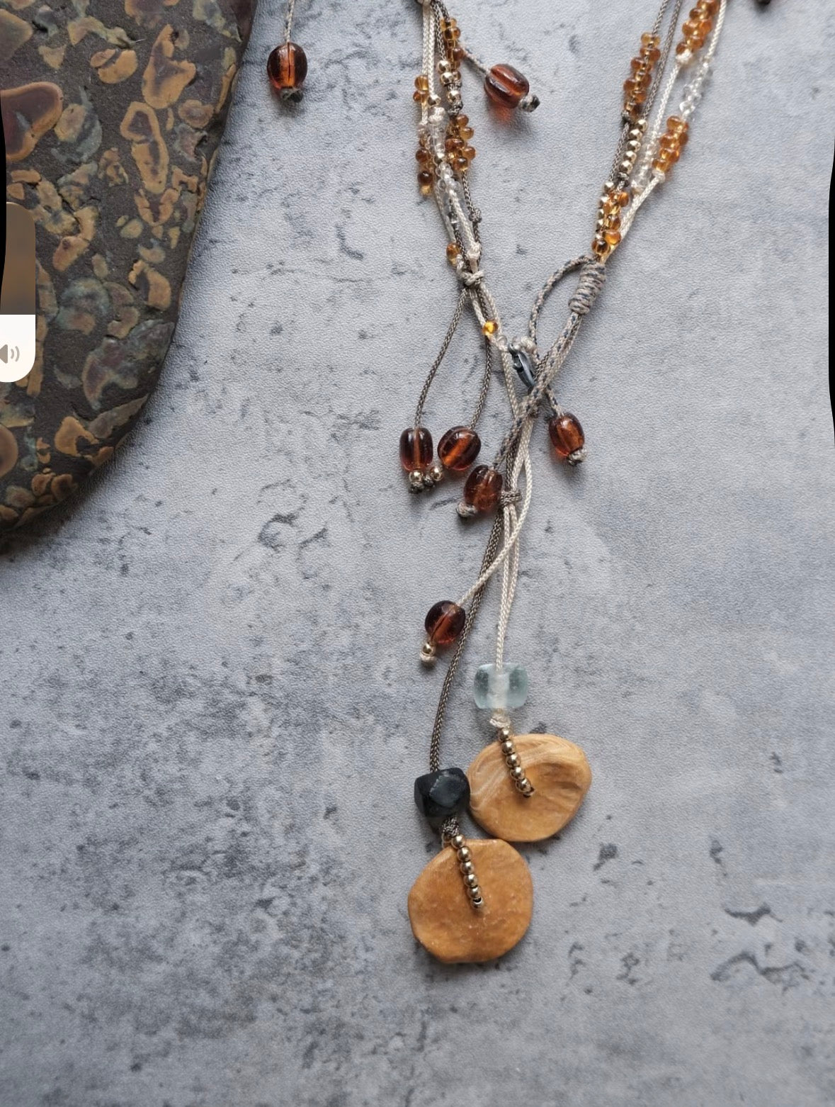 Detail view of a handmade brass pendant necklace with cord and bead accents.