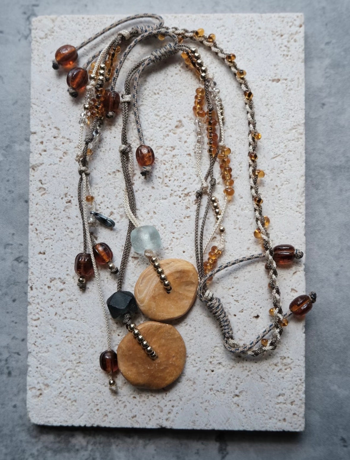 Handmade brass pendant necklace with layered cords, mixed beads, and metal details.