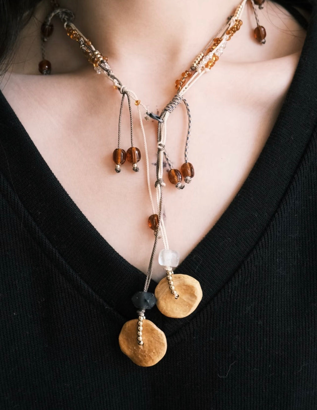 Model wearing a handmade brass pendant necklace with layered cord details and mixed beads.