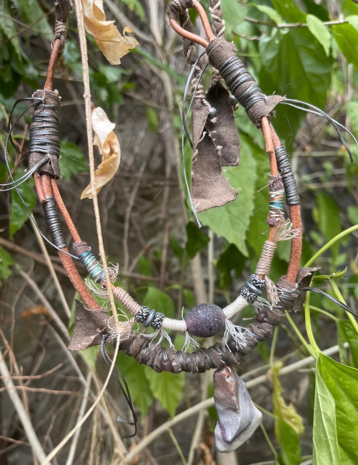 Handmade rustic pendant necklace displayed outdoors among natural textures