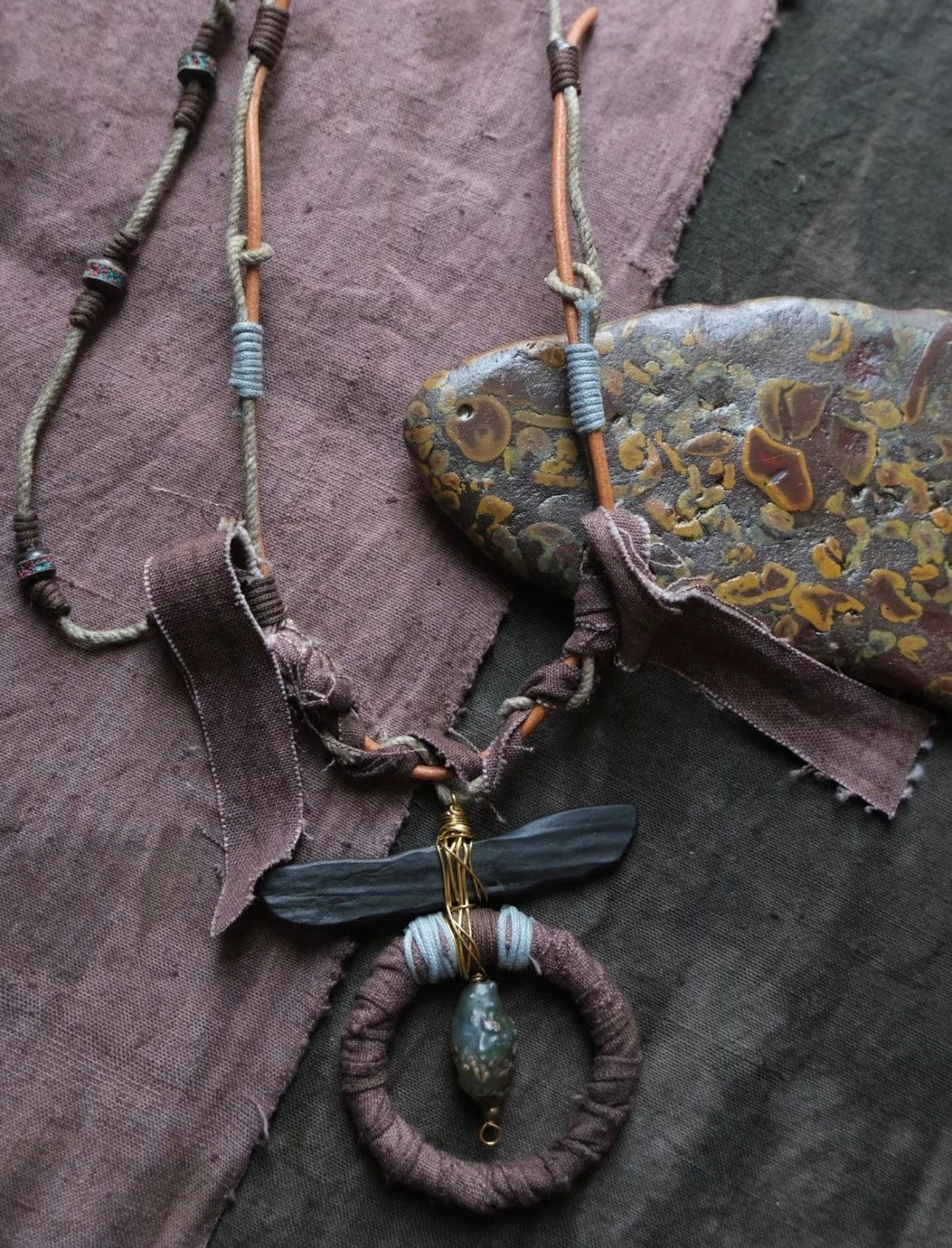 Model wearing a one-of-a-kind handmade statement necklace in earthy boho style with textile details and artisan pendant design