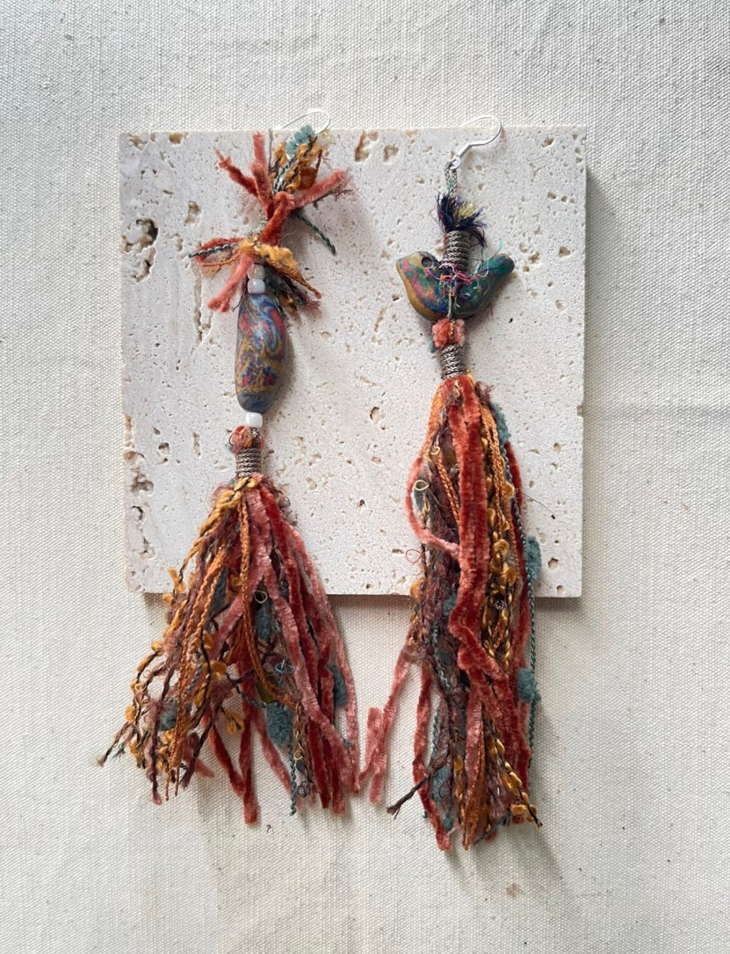 Handmade bird tassel earrings with layered textile fibers and asymmetrical detail.