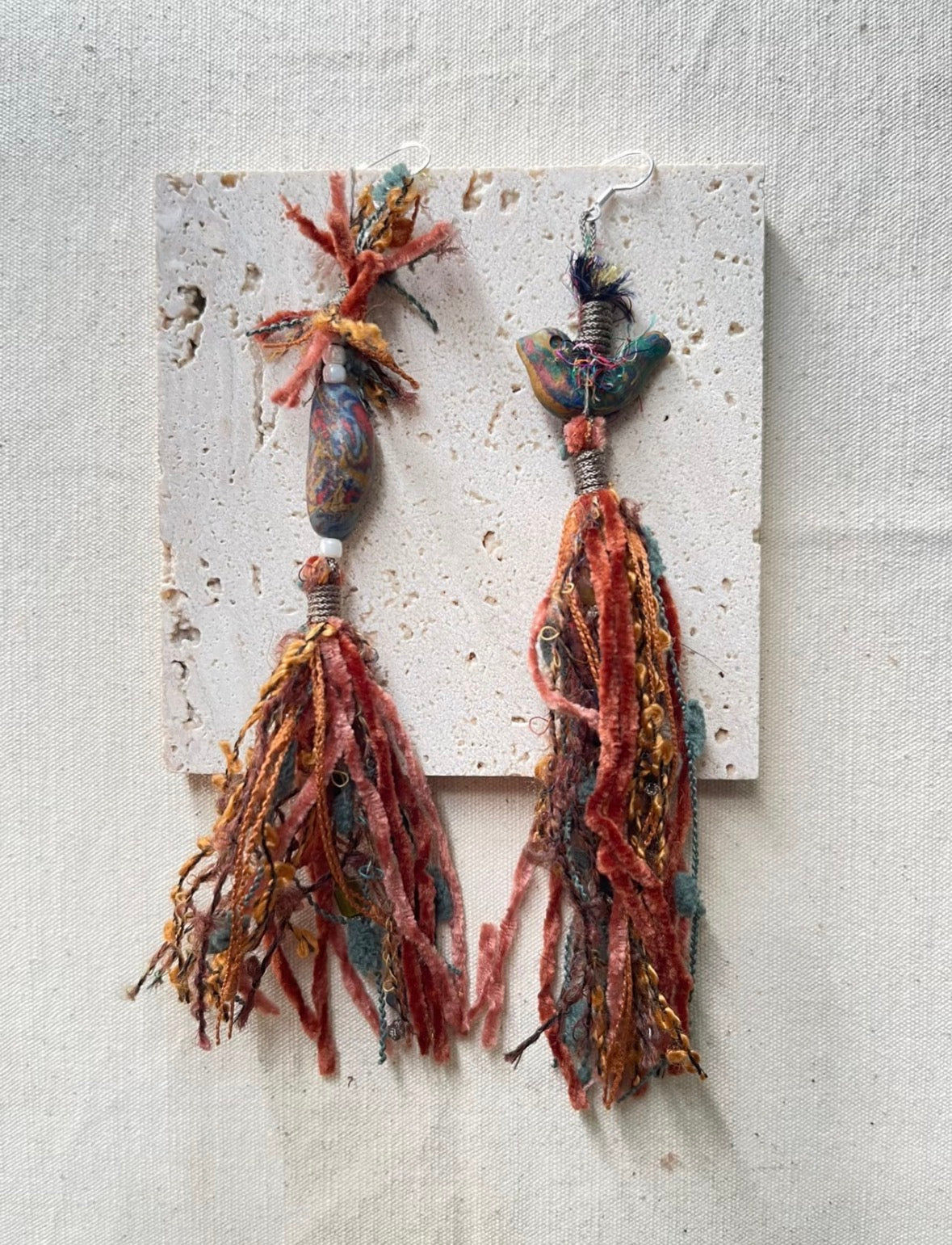 Handmade bird tassel earrings with layered textile fibers and asymmetrical detail.