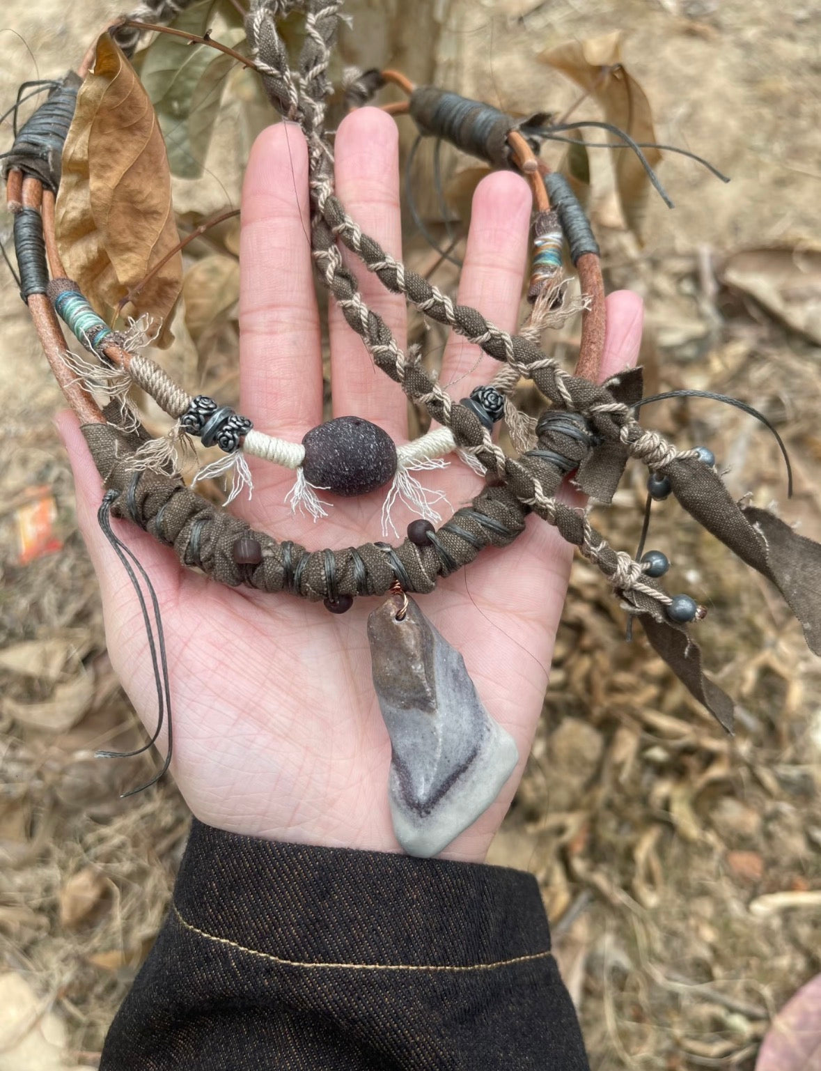 Rustic pendant necklace shown in hand with layered cord and bead details